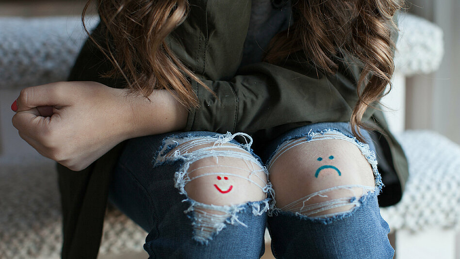 Meist lässt sich keine eindeutige Ursache für ein Sarkom ausmachen. Ein fröhlicher und ein trauriger Smiley auf den Knien einer Frau